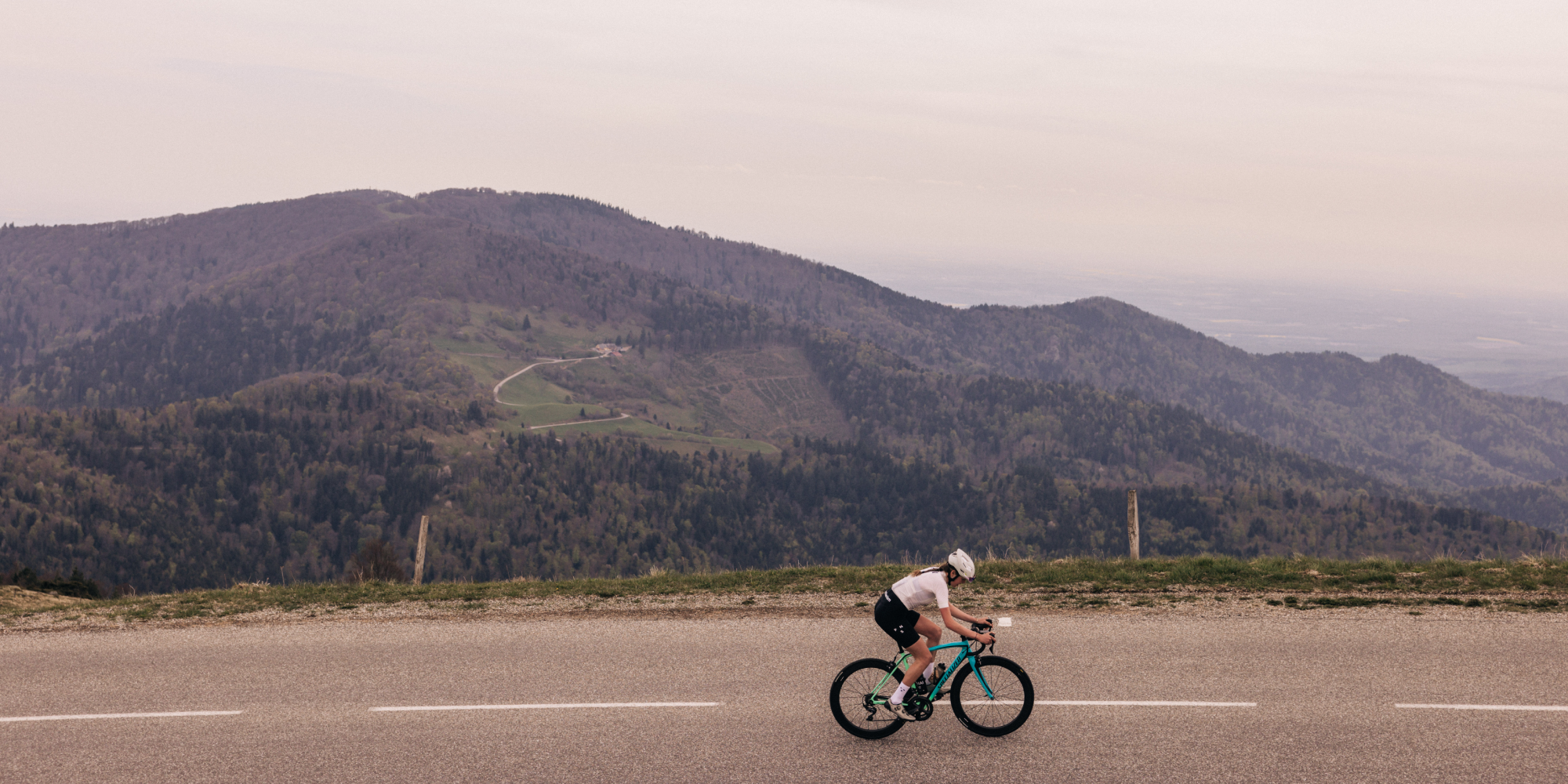 Female cyclist rides along a road with hills in the background