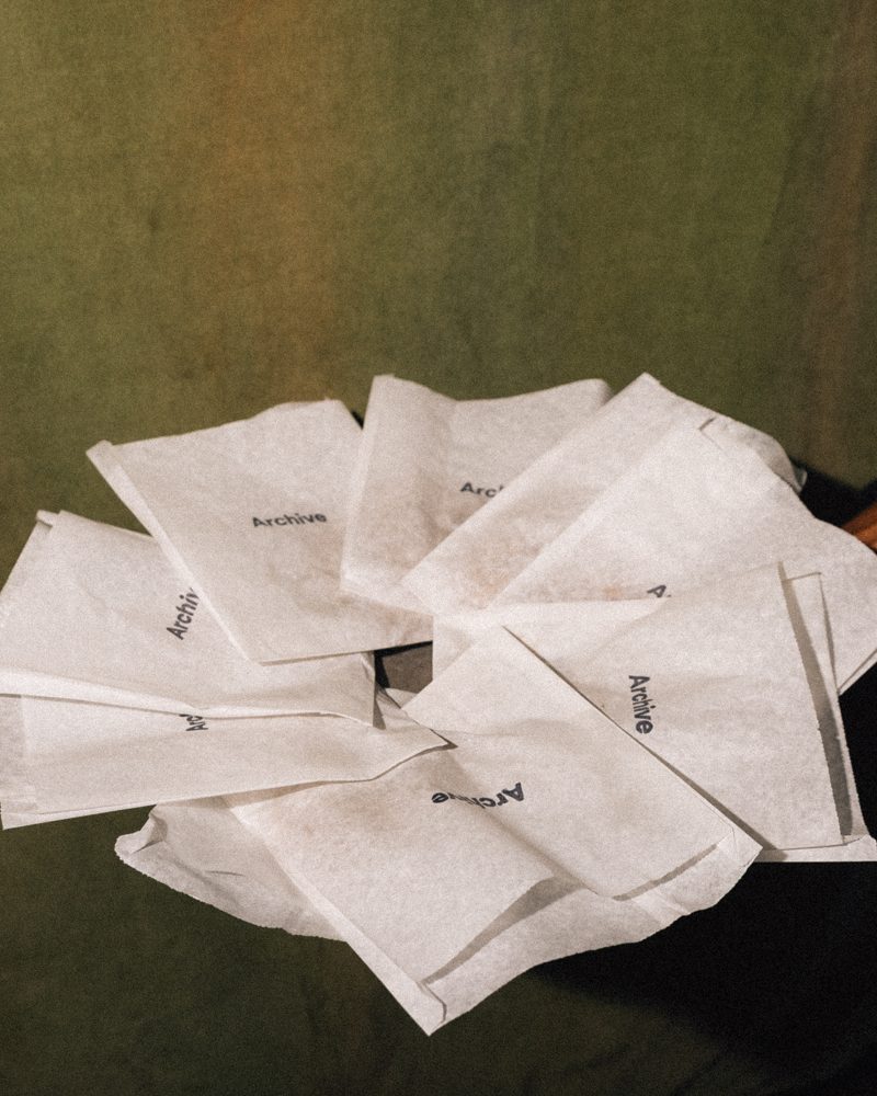 A hand holding a stack of paper pastry bags printed with the Archive wordmark