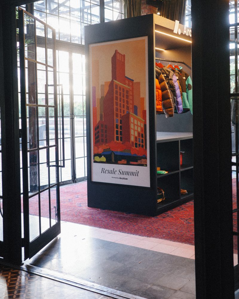 The Archive resale display at the Resale Summit, with a Resale Summit poster and a rack of secondhand jackets